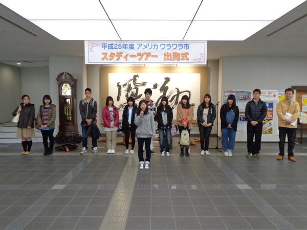 出発式にて、荷物を持って並ぶ男女の高校生とその前でマイクを持って話をしている女子生徒の写真